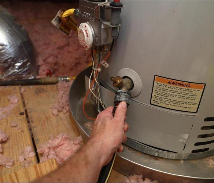 Hand attaches hose to a home water heater to perform maintenance